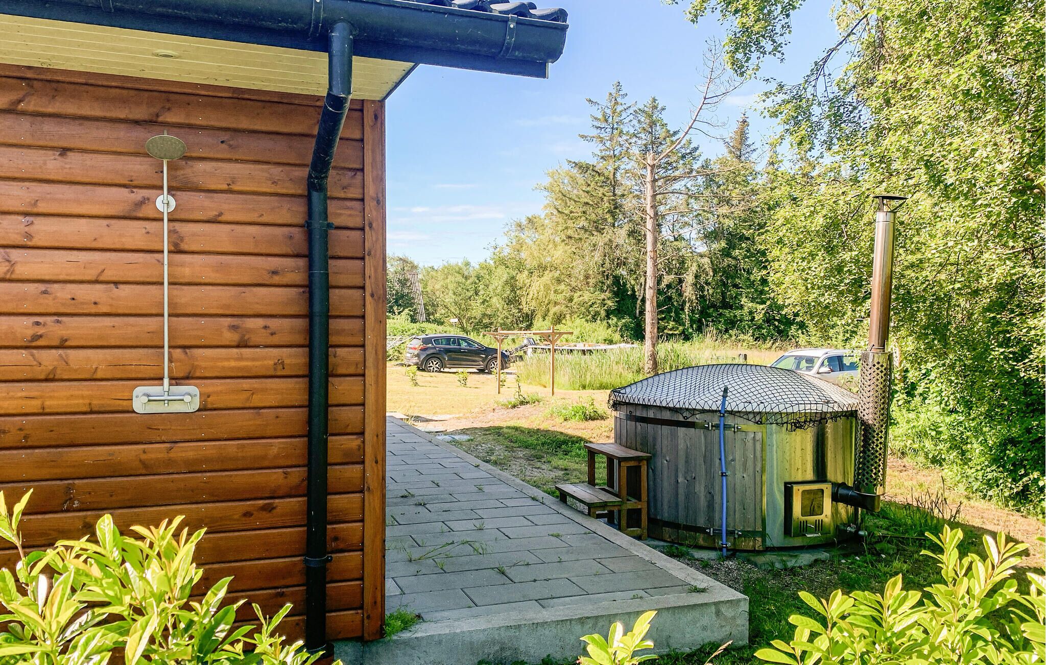 Een houten chalet met een metalen dak, een kleine houten tuinhuisje en een geplaveid pad dat naar een auto op de achtergrond leidt.