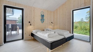 Un dormitorio moderno con una cama grande, paredes de madera y vistas al verde.