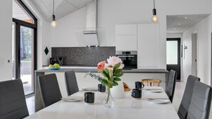 Una cocina moderna con un salpicadero de azulejos negros, una isla central y un comedor con una mesa blanca y sillas negras.