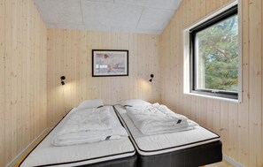 Una habitación con dos camas, paredes de madera, un cuadro enmarcado y una ventana con vista a árboles.