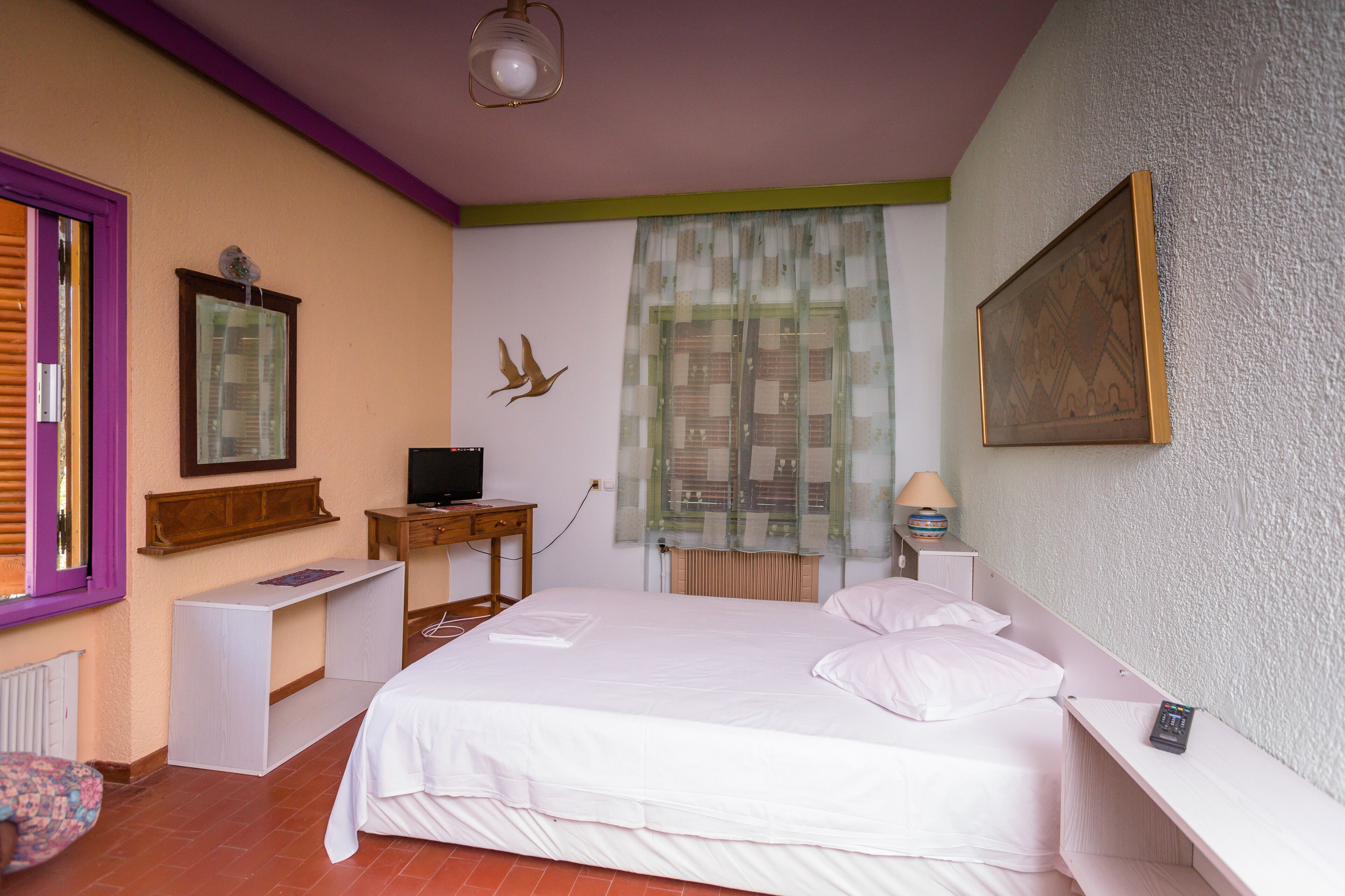 A bedroom with a bed, a desk, a chair, a television, and a window with curtains.