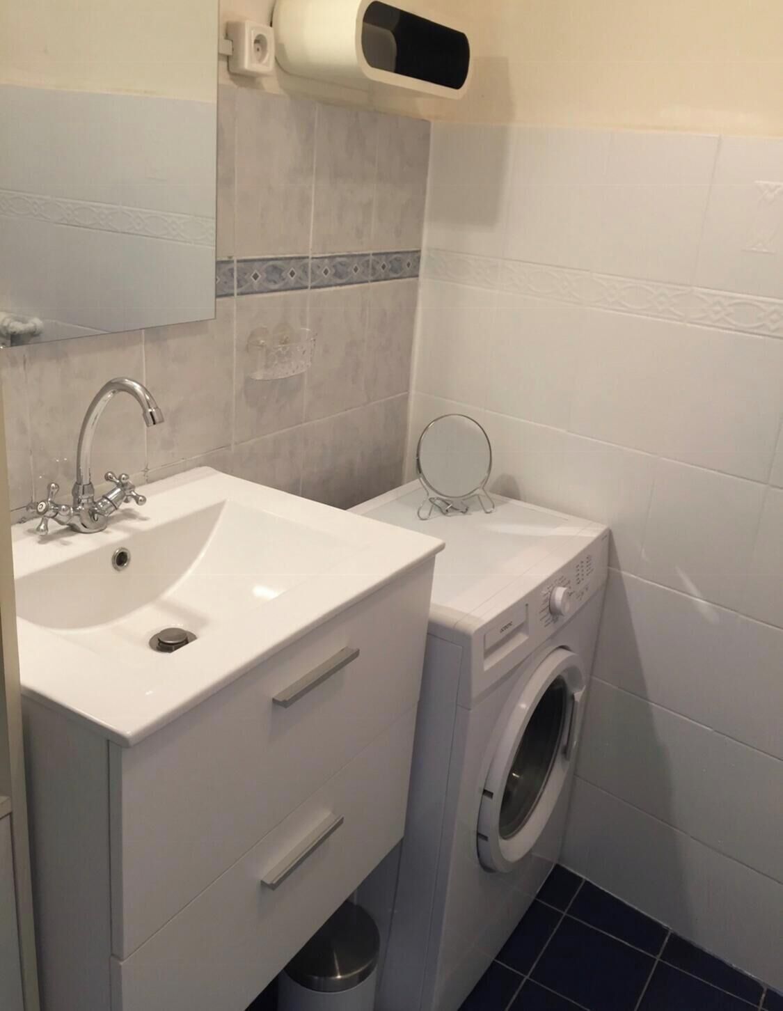 A compact bathroom with a white sink, a built-in washing machine, and a mirror above the sink.