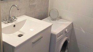 Ett litet badrum med ett vitt handfat, en inbyggd tvättmaskin och en spegel ovanför handfatet.