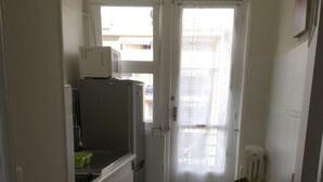 Ett kompakt kök med kylskåp, diskho och ett litet matbord med en stol.