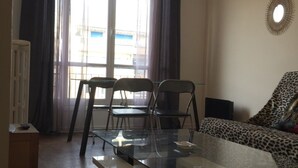 Ett vardagsrum med ett soffbord med glasskiva, två stolar, en soffa med ett leopardmönstrat överdrag, ett element och ett fönster med gardiner.