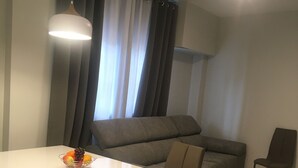 Una sala de estar moderna con una mesa blanca, un sofá gris y una mesa de centro de vidrio con fruta.