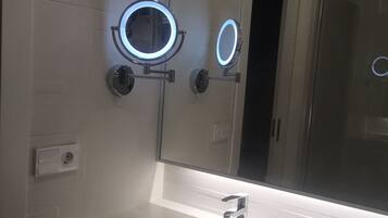 A bathroom with a white sink, a mirror with two illuminated lights, and a towel rack.