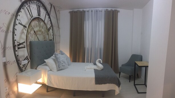 Un dormitorio con una cama, un reloj de pared grande, una silla y una mesita.