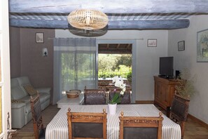 A cozy living room with a sofa, a dining table with chairs, a television, and a view of greenery outside.