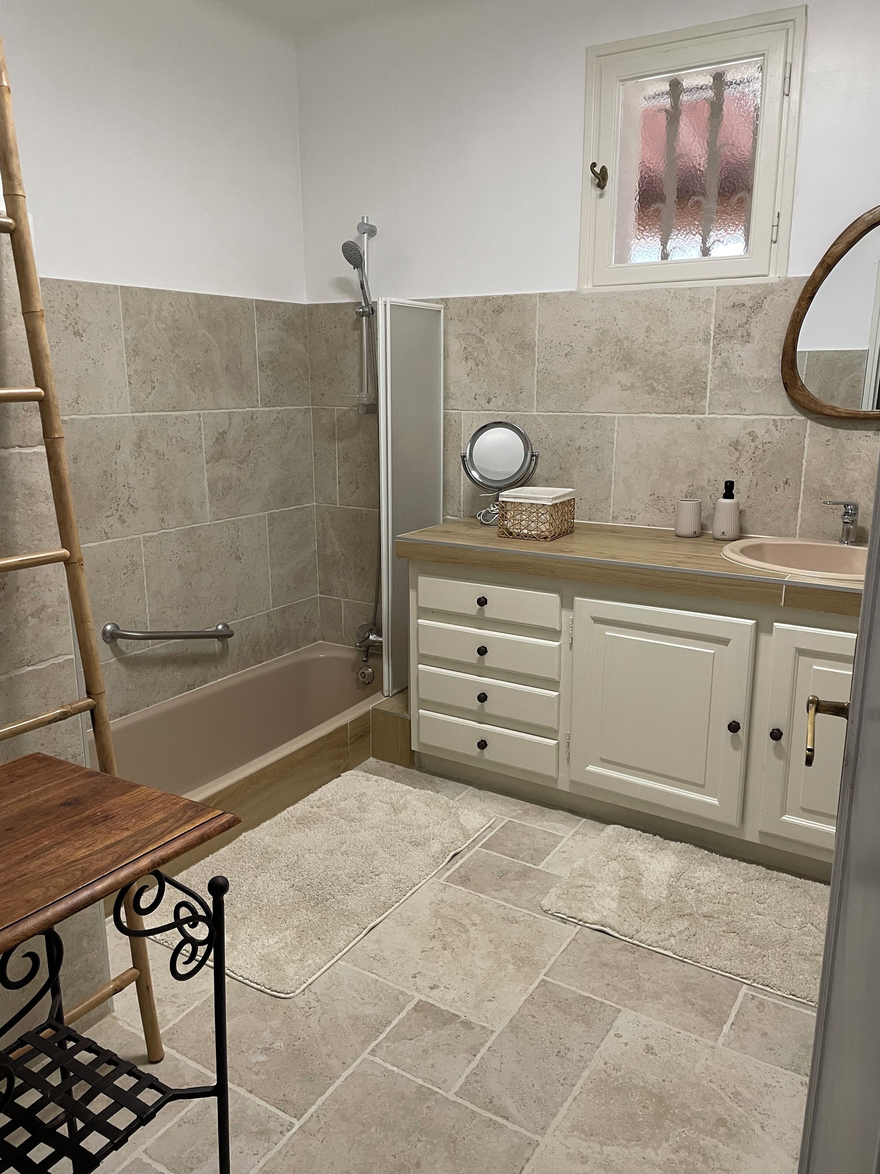 A bathroom with a bathtub, a shower, a vanity with a mirror, and a wooden bench.