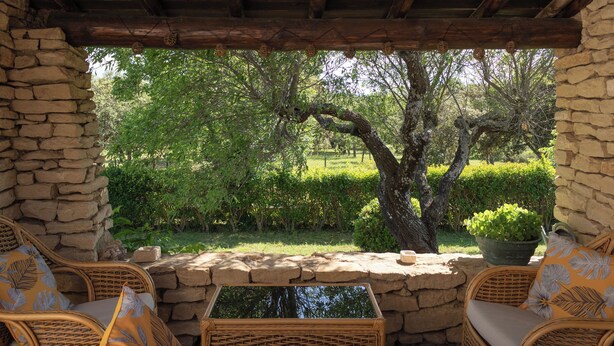 A stone-walled patio with wicker furniture and a view of a lush garden. - Villa Provencale Face AU Luberon (Cabrières-d'Avignon)