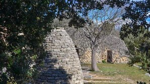 A stone structure with a conical roof, surrounded by trees and grass. - Villa Provencale Face AU Luberon (Cabrières-d'Avignon)