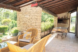 A stone wall with wicker furniture and a table under a wooden roof.