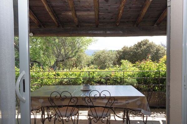 An outdoor patio with a table and chairs, surrounded by a metal railing and lush greenery.