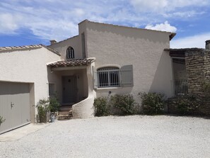 A two-story house with a gravel driveway, a front door, and a small window with shutters.