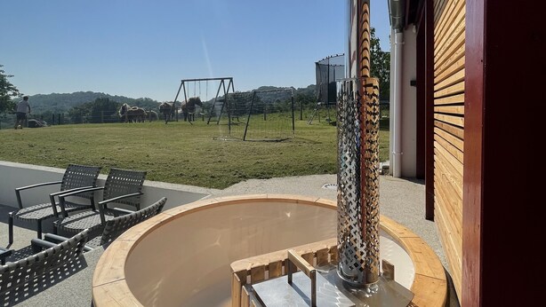 Ein kreisförmiger Außenbereich mit Sitzgelegenheiten, ausgestattet mit einer Feuerstelle in der Mitte, einer Holzterrasse und Metallstühlen.