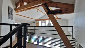 Ein modernes Interieur mit freiliegenden Holzbalken, einer schwarzen Metalltreppe und Blick auf einen Poolbereich im Freien.
