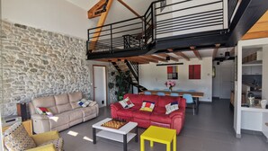 Ein großzügiger Wohnbereich mit Steinwand, einem roten Sofa, einem gelben Sessel und einem Schachbrett auf einem weißen Couchtisch.