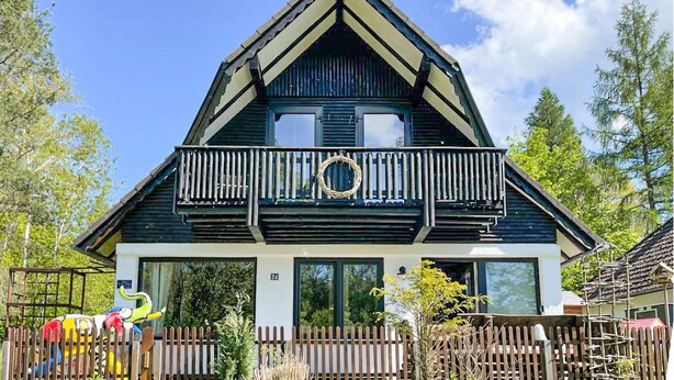 En traditionel chalet-bygning med balkon, store vinduer og et træhegn.
