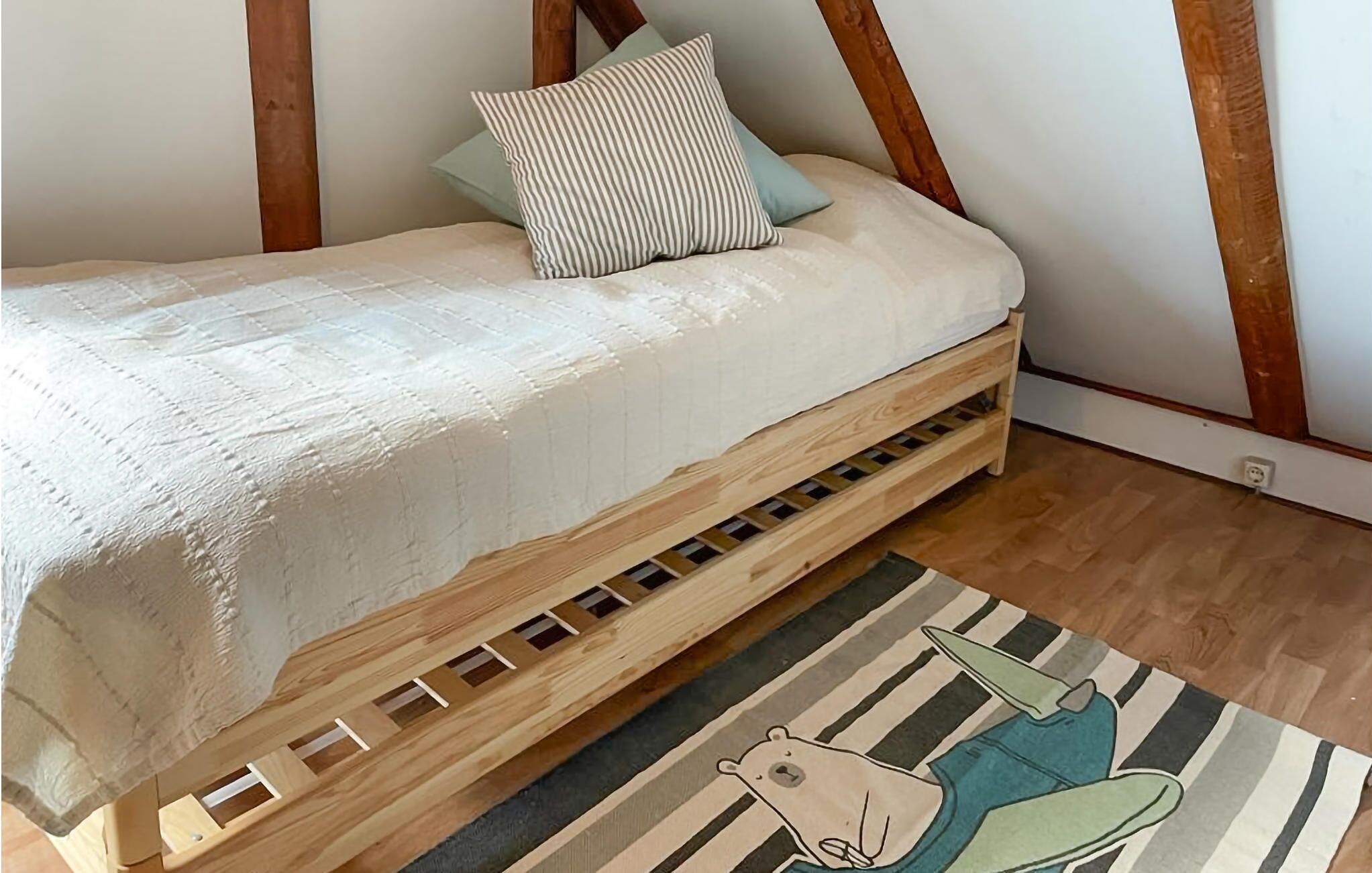 A wooden loft bed with a mattress and pillows, a striped rug, and a wooden floor.
