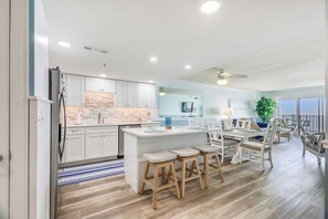 Una cocina moderna con armarios blancos, una isla central con taburetes y un comedor con sillas blancas.