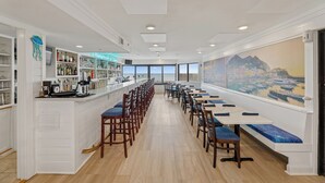 Un amplio comedor con mesas y sillas altas, un bar a la izquierda y un ventanal con vistas a la ciudad.
