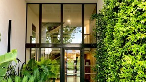 A modern building entrance with a glass door, surrounded by lush greenery and a gravel pathway. - Haven of peace with infinity pool overlooking the sea (Villeneuve-Loubet)