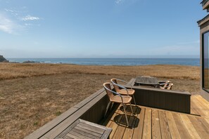 Una terraza de madera con una mesa y sillas que da a un paisaje costero.
