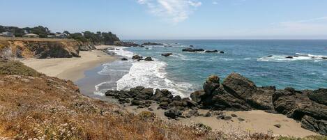 A coastal landscape with a beach, rocky shoreline, and ocean waves.