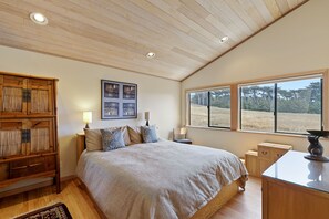 Un dormitorio con una cama grande, un armario de madera, mesitas de noche, un escritorio y una ventana con vistas a árboles.
