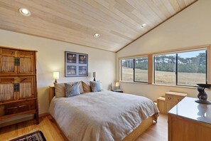 A bedroom with a large bed, wooden wardrobe, bedside tables, a window with a view of trees, and a ceiling with recessed lighting.
