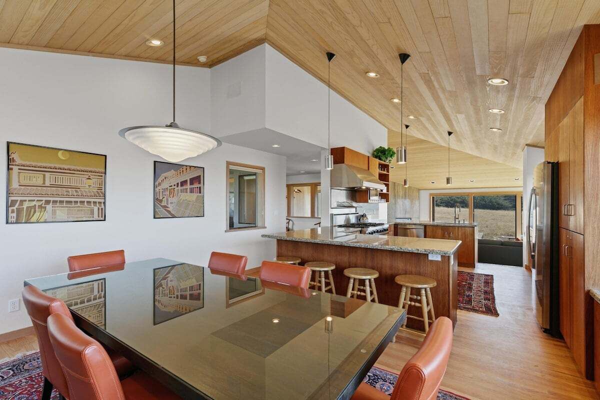 A modern kitchen with a central island, wooden cabinets, and a dining area with a glass table and leather chairs.