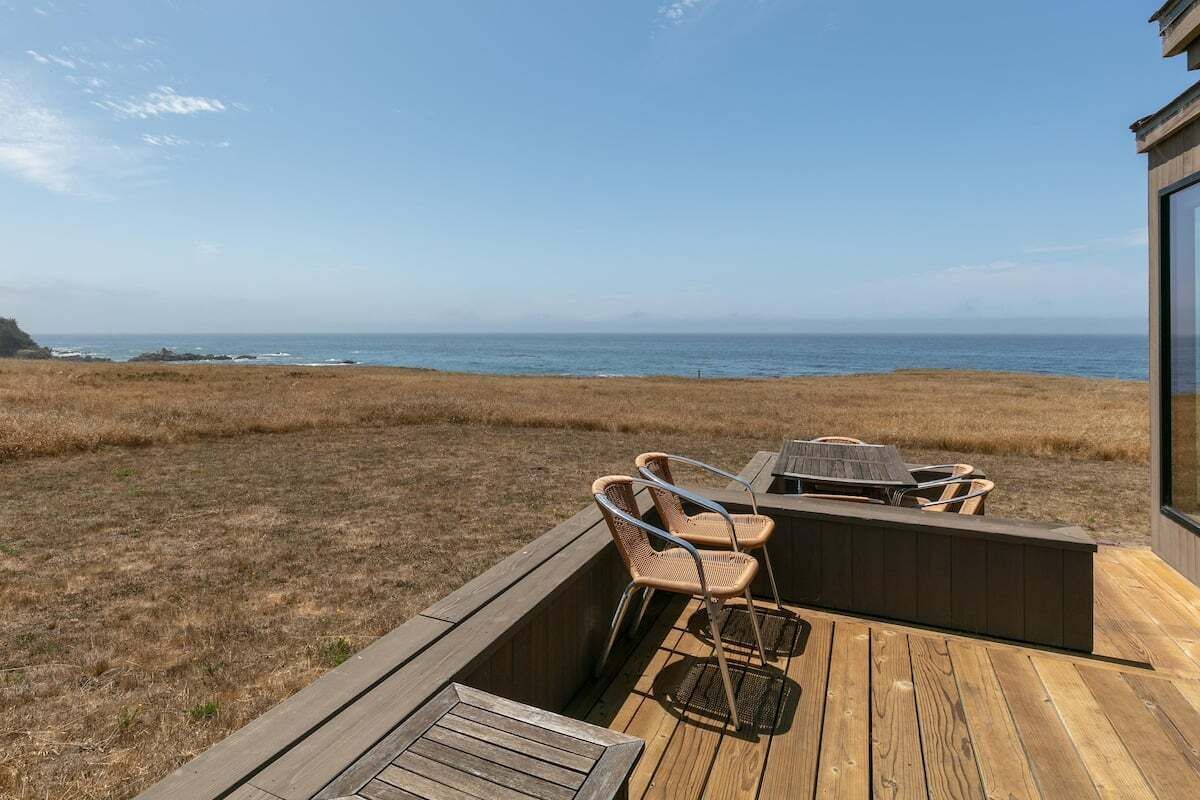 Terraza de madera con mobiliario exterior, con vista al paisaje costero.