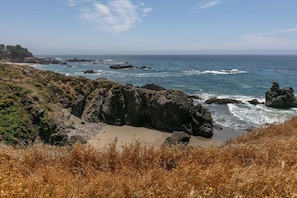 A coastal landscape with rocky terrain, a sandy beach, and the ocean. - Kyuka | Asian-Inspired Coastal Retreat (Sea Ranch)