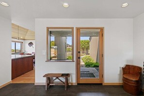 A modern interior with a wooden bench, a bench with a plaque, a wooden chair, and a door leading to an outdoor area. - Kyuka | Asian-Inspired Coastal Retreat (Sea Ranch)