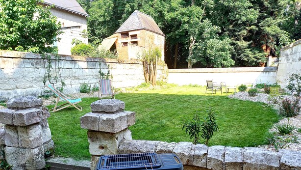 Eine Terrasse mit Grill, Steinstufen und einem Rasen.