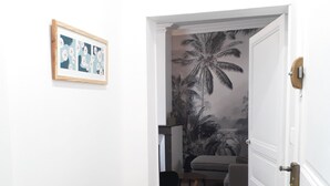 Ein Flur mit einer weißen Tür, die in einen Wohnbereich mit einer Couch und einer Wandmalerei führt.