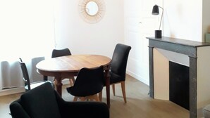 En matplats med ett runt träbord, svarta stolar, ett litet sidobord och en öppen spis.