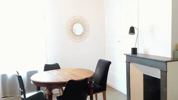 Un coin repas comprenant une table ronde en bois, des chaises noires, une petite table d’appoint et une cheminée.