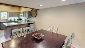 A kitchen with a wooden dining table, chairs, and a clock on the wall. - Snowcreek Resort Vacation Rental 480 (Mammoth Lakes)