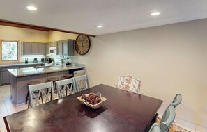 A kitchen with a wooden dining table, chairs, and a clock on the wall. - Snowcreek Resort Vacation Rental 480 (Mammoth Lakes)