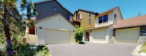 A residential area with multiple detached houses, each with a garage, surrounded by trees and a clear sky.