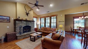 A living room with a stone fireplace, leather sofa, and a dining area with wooden chairs.