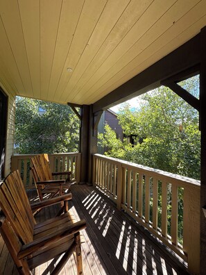 A wooden deck with a railing, two wooden chairs, and a view of greenery and a house in the background.