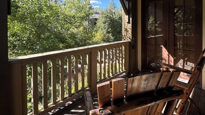 A wooden deck with a railing, two wooden chairs, and a view of greenery and a building in the background. - Snowcreek Resort Vacation Rental 1135 (Mammoth Lakes)