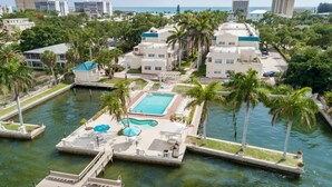 A resort with a central swimming pool, connected walkways, and palm trees.