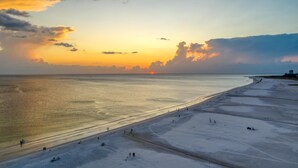 A wide beach with a clear view of the ocean and a sunset in the background.