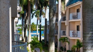 A hotel courtyard with palm trees, a pool, and a building with balconies.
