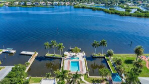 An aerial view of a waterfront property with a central swimming pool, docked boats, and lush greenery.