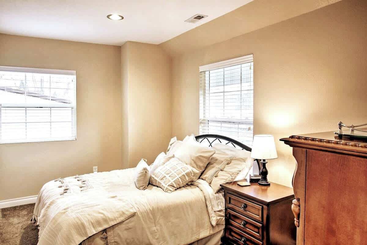 A bedroom with a bed, dresser, nightstand, and two windows.